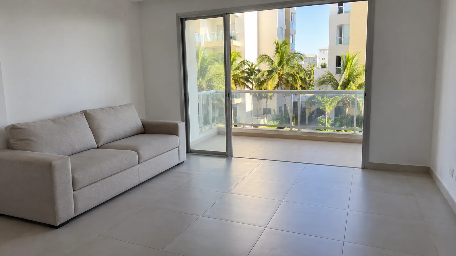 Sala vacía de un apartamento modelo con piso de cerámica y balcón con palmeras